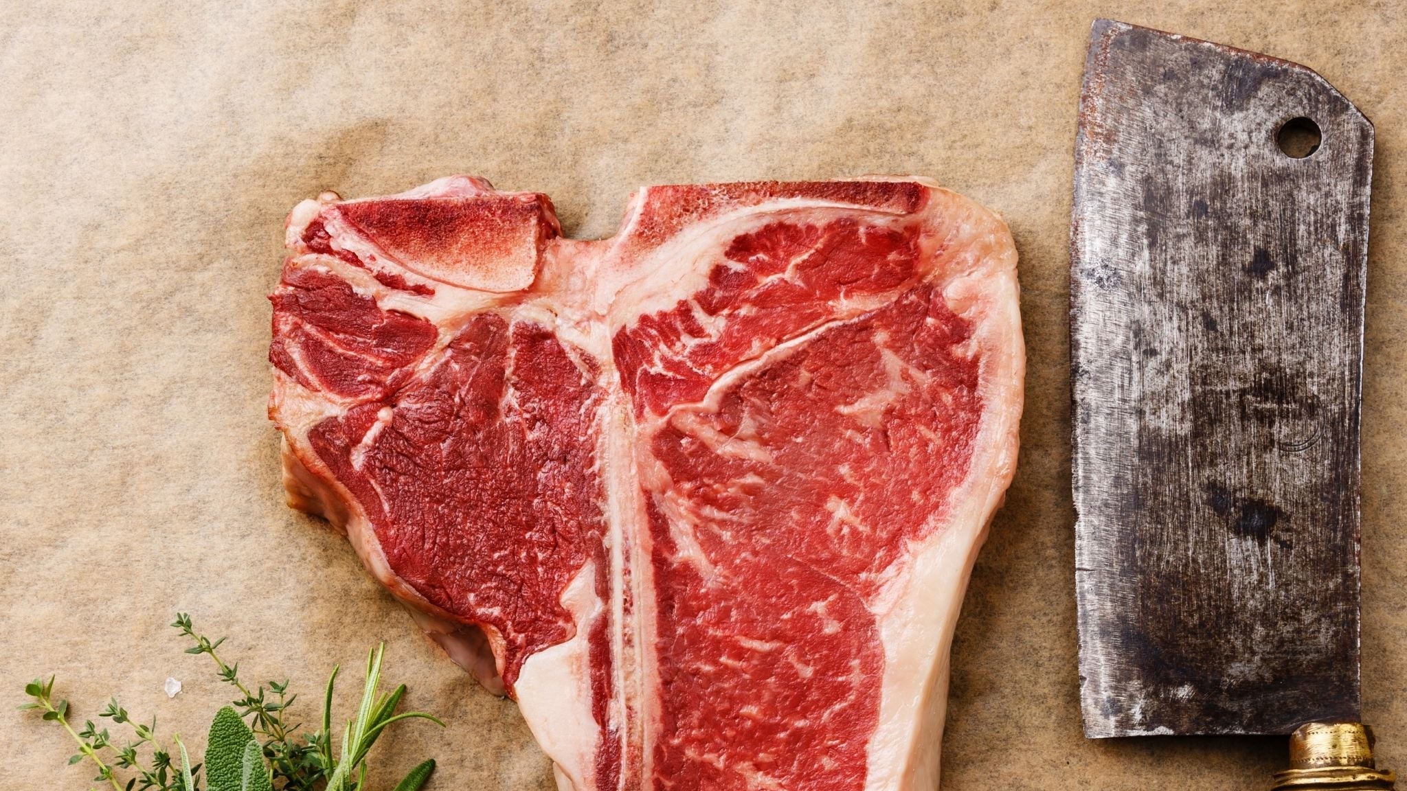 Raw steak with herbs, peppers, garlic, and a cleaver on a rustic background